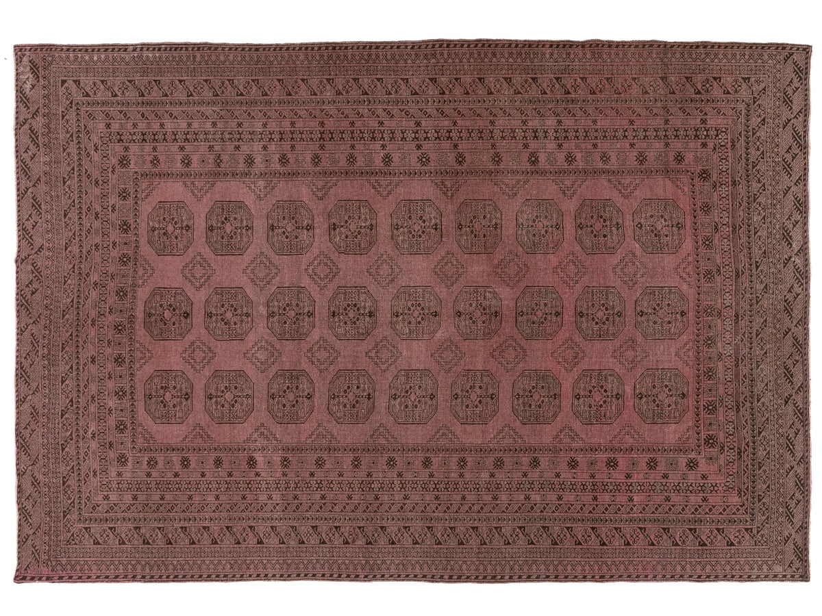 A rectangular vintage rug with a dusty rose and dark brown geometric pattern, featuring a central field of medallions and a detailed border.