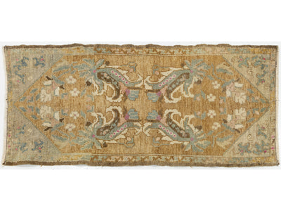 A vintage rectangular area rug with a faded tan and beige base, featuring a symmetrical floral and scroll pattern in muted blue, green, pink, and brown tones.