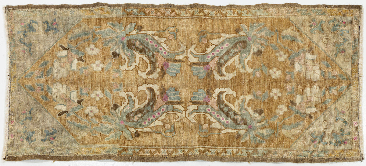A vintage rectangular area rug with a faded tan and beige base, featuring a symmetrical floral and scroll pattern in muted blue, green, pink, and brown tones.