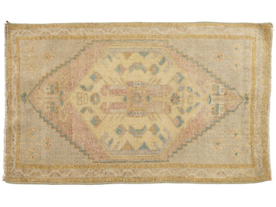 A vintage rectangular area rug with a faded beige background and a central diamond medallion pattern in muted pink, cream, and blue-green tones.