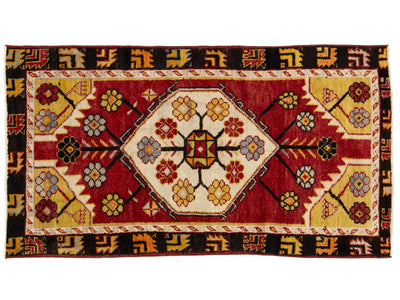A rectangular vintage patterned rug with a central medallion design. The rug features a deep red field, cream-colored borders, and yellow, black, and blue floral motifs.