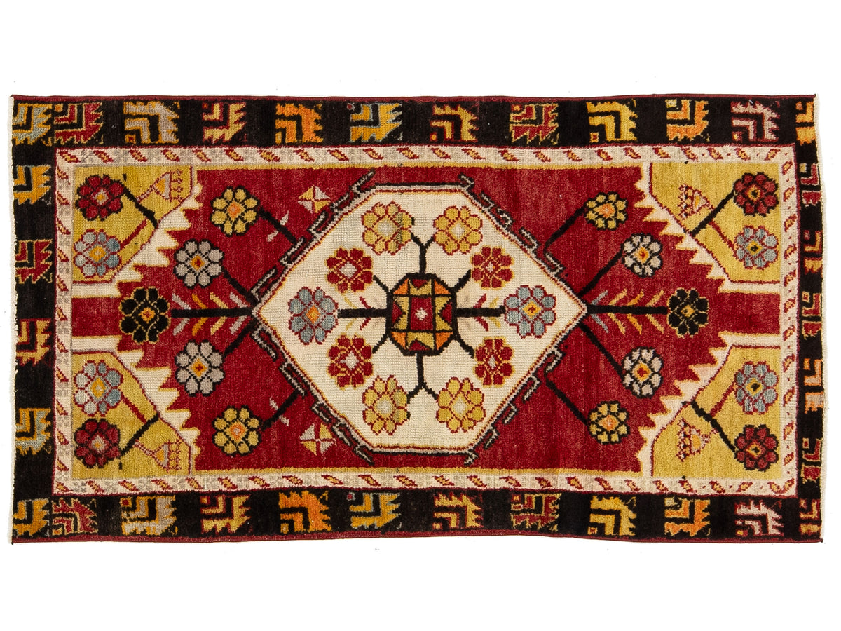 A rectangular vintage patterned rug with a central medallion design. The rug features a deep red field, cream-colored borders, and yellow, black, and blue floral motifs.