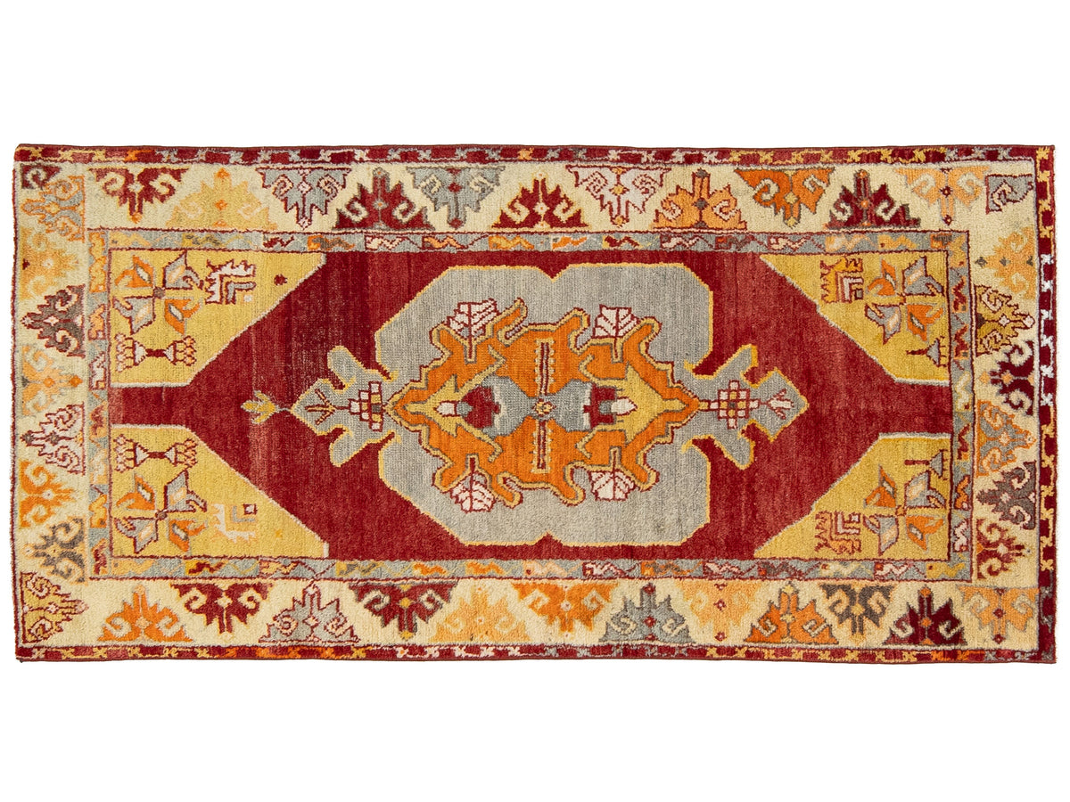 A rectangular hand-knotted area rug with a traditional geometric pattern, featuring a central medallion in rust red, orange, and beige, surrounded by a matching patterned border.