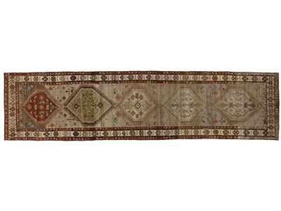 An antique Persian runner rug with intricate geometric and floral motifs in muted red, beige, brown, and blue tones.