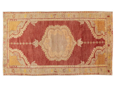 A rectangular vintage area rug with a central medallion design in muted red, beige, and ochre yellow tones, shown flat against a white background.