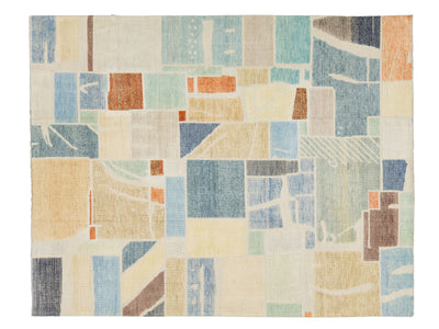 An abstract geometric area rug featuring a patchwork design of blocks and textured panels in muted shades of blue, beige, cream, orange, and brown.