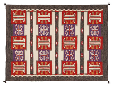 A rectangular woven rug with a Southwestern geometric pattern, featuring red, purple, cream, and brown blocks with white and red stylized symbols.