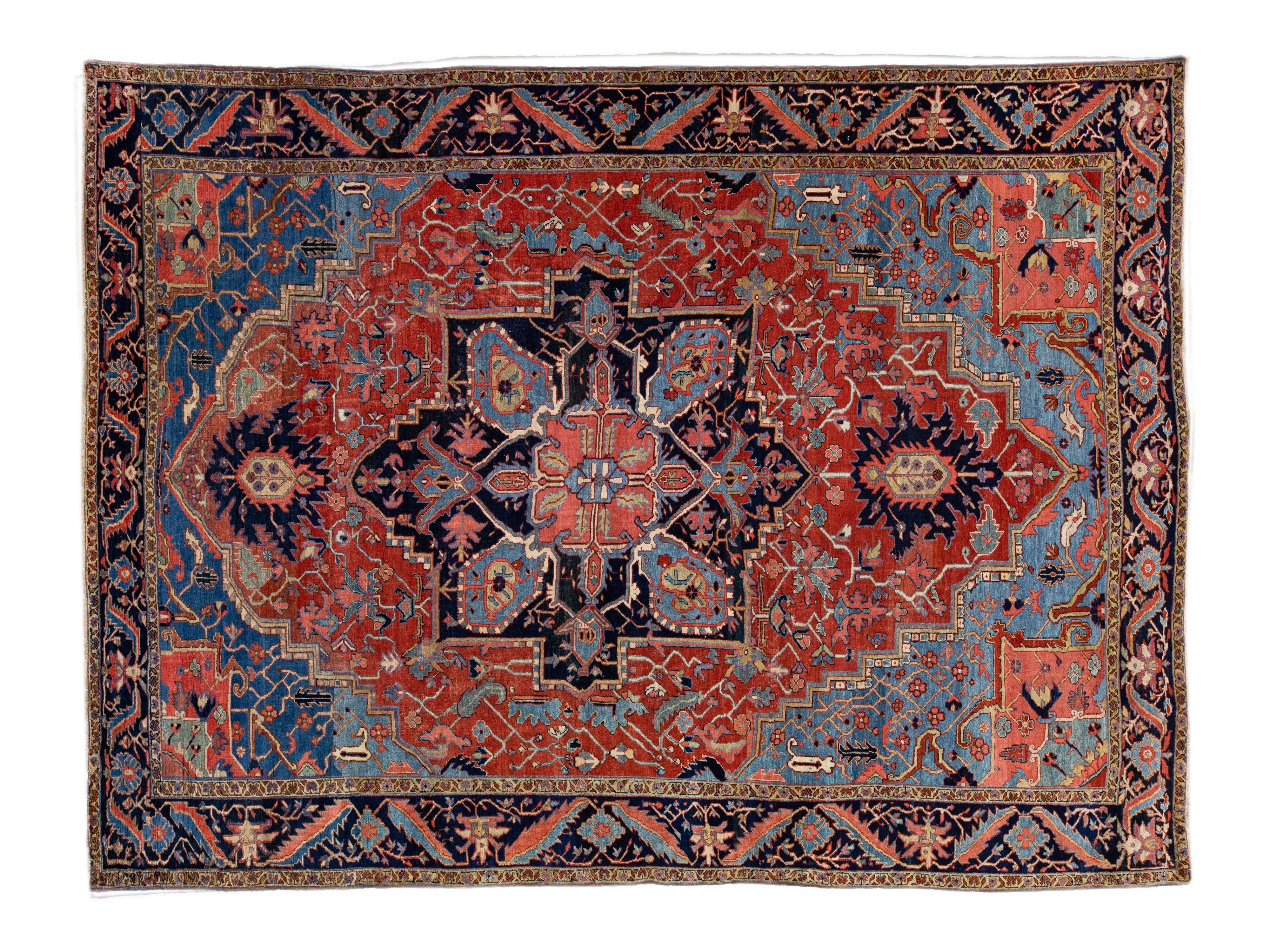 A traditional Persian-style area rug with a complex geometric and floral medallion pattern, featuring a dominant red field, a dark navy blue central medallion, and a blue and red border.