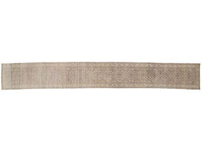 A runner rug with an intricate traditional pattern in muted beige, gray, and brown tones, shown flat against a white background.