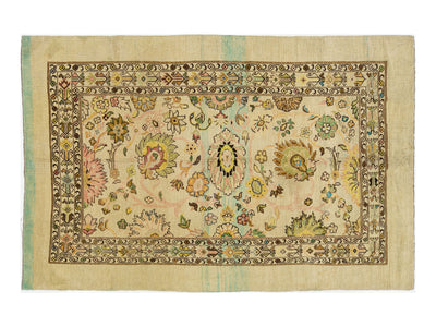 Hand-knotted wool rug with a cream-colored field, featuring a central floral medallion and a detailed border in muted tones of green, pink, yellow, and brown.