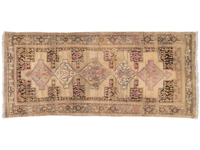 A vintage Persian area rug with a beige base, featuring a central row of large pink and blue diamond medallions and a detailed geometric border.