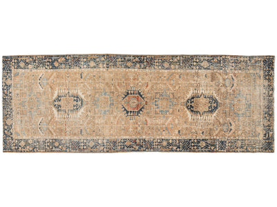 A rectangular vintage area rug with a distressed beige field, navy blue borders, and central medallions in muted red, blue, and cream.