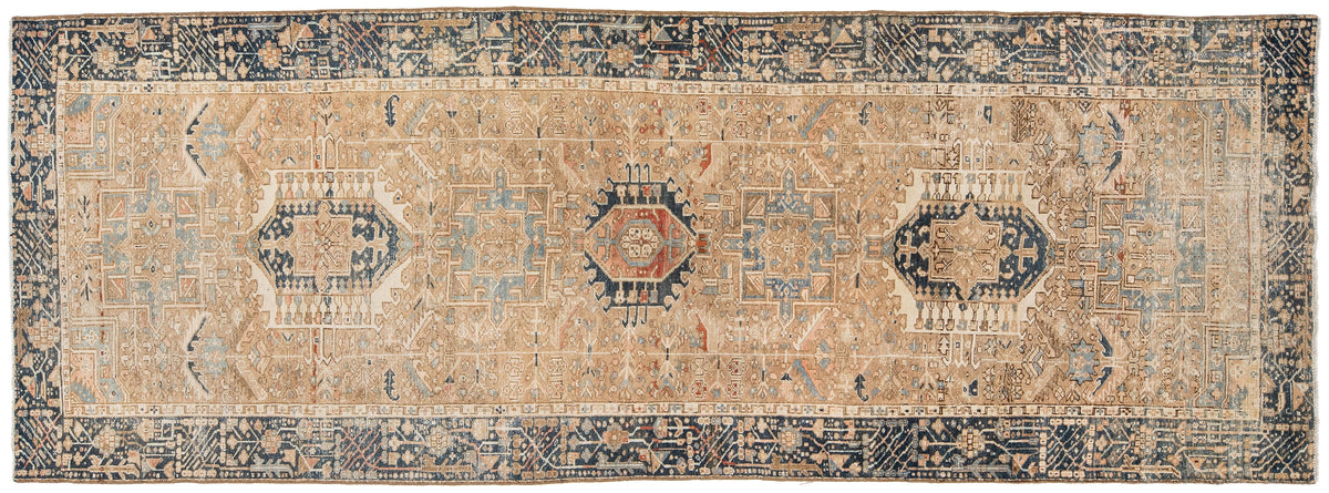 A rectangular vintage area rug with a distressed beige field, navy blue borders, and central medallions in muted red, blue, and cream.