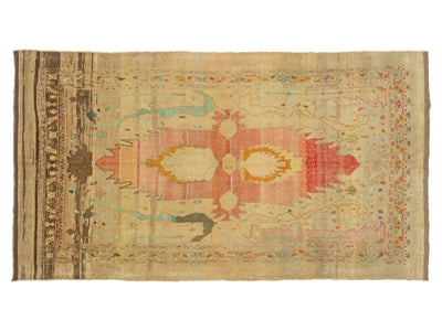 A flat-laid vintage-style area rug with a distressed, hand-knotted texture. The rug features a central medallion motif in muted shades of pink, ochre yellow, and light blue on a warm beige background, framed by a brown patterned border on the left side.