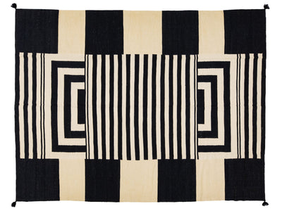 A rectangular woven rug with a bold geometric pattern in black and cream, featuring vertical stripes, concentric rectangular loops, and solid color blocks.