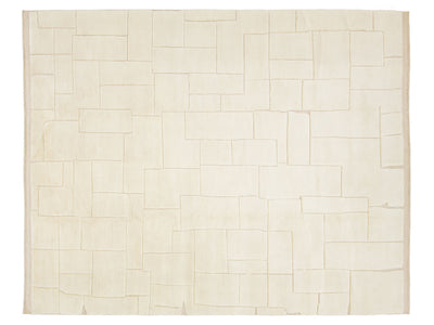 A rectangular cream-colored rug with an abstract geometric pattern of stitched rectangular blocks outlined in a light tan thread.
