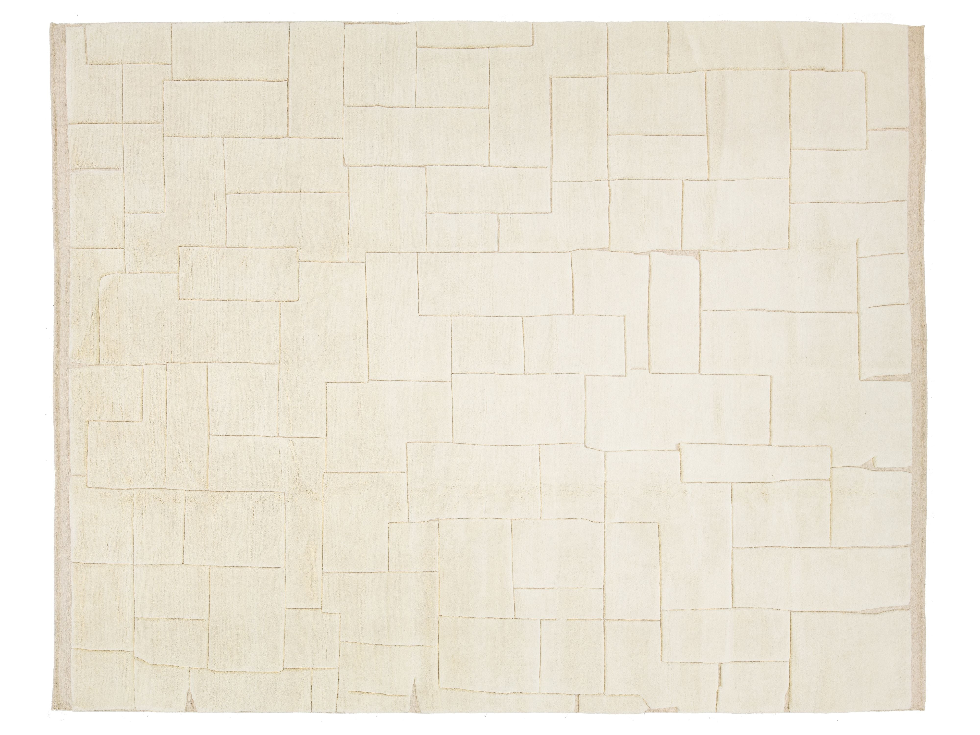 A rectangular cream-colored rug with an abstract geometric pattern of stitched rectangular blocks outlined in a light tan thread.