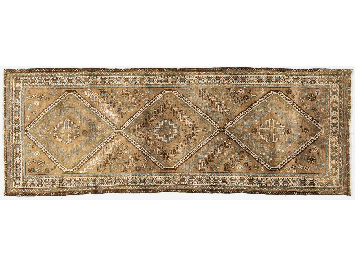 A vintage runner rug with a distressed, vintage appearance. The rug features three large central diamond medallions and an intricate patterned border, in muted tones of brown, beige, and gray.