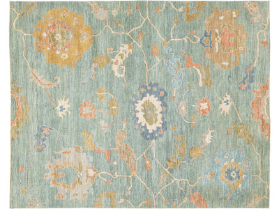 A rectangular area rug with a traditional pattern in muted tones of sage green, mustard yellow, dusty blue, and cream.