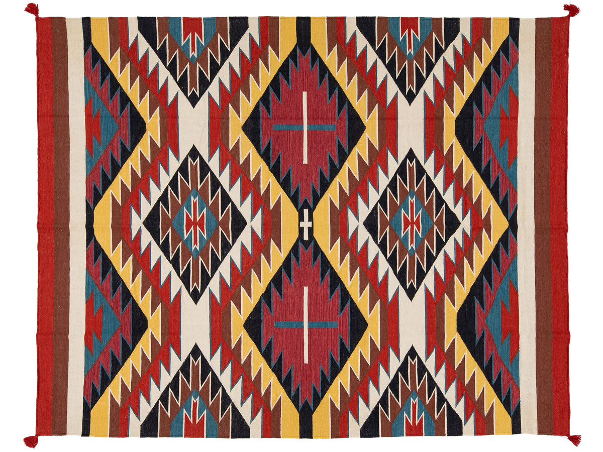 A rectangular woven rug with a bold Southwestern geometric pattern in red, yellow, black, blue, and cream, featuring diamond motifs and zigzag borders.
