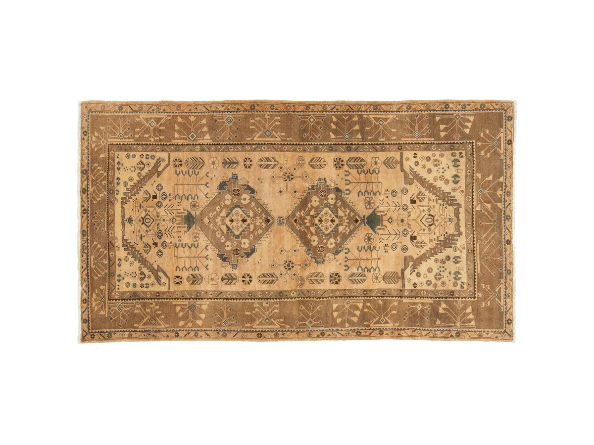 A vintage area rug with a distressed geometric pattern in warm tan, beige, and brown tones, featuring two central medallions and intricate border details.