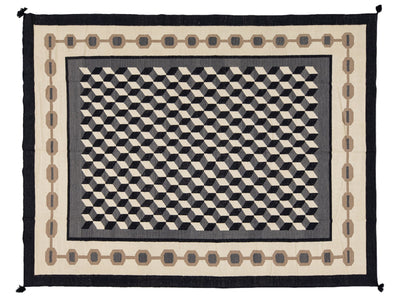 A rectangular woven rug with a bold black, gray, beige, and brown geometric pattern, featuring a central 3D-effect cube motif and an ornate border.
