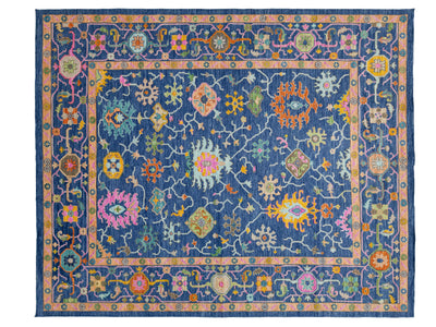A rectangular traditional-style area rug with a navy blue field, pink border, and intricate multicolored floral and geometric motifs throughout.