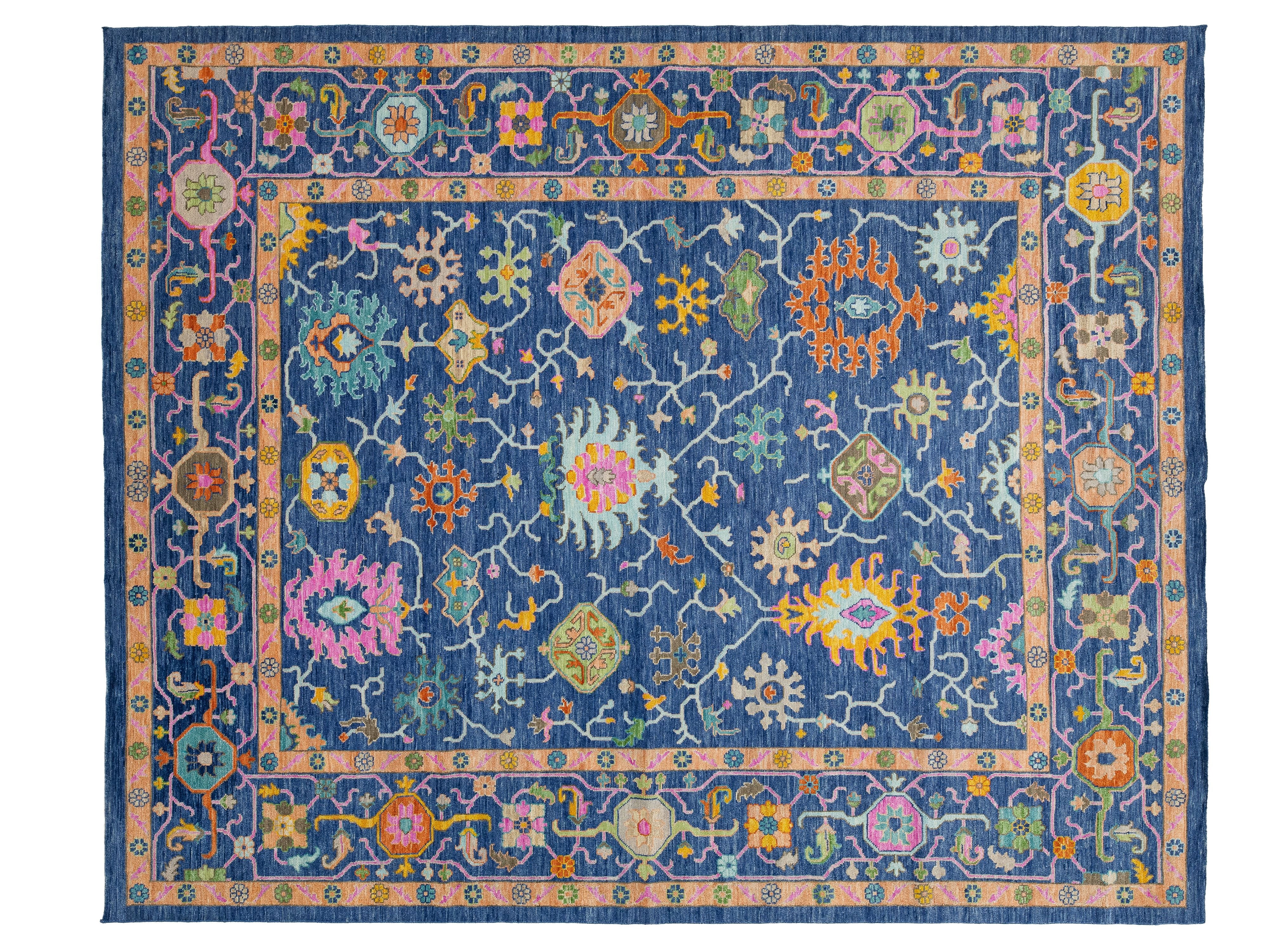 A rectangular traditional-style area rug with a navy blue field, pink border, and intricate multicolored floral and geometric motifs throughout.