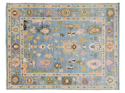 A rectangular area rug with a light blue central field and a detailed multicolor border and medallion pattern, shown flat against a white background.