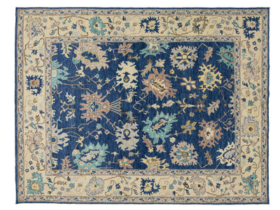 A rectangular traditional area rug with a navy blue central field, surrounded by a beige border and detailed floral motifs in blue, beige, and light teal.