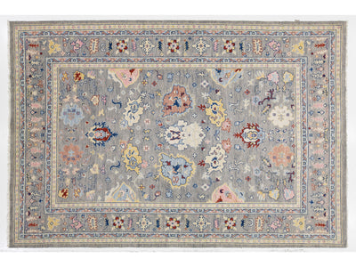 A rectangular area rug with an intricate traditional floral pattern, featuring a light gray-blue field and a detailed border in muted shades of pink, blue, beige, and red.