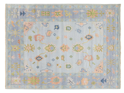 A rectangular area rug with a light blue-gray field and border, decorated with intricate floral and geometric motifs in pastel pink, sage green, soft yellow, and touches of blue.