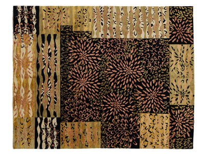 A rectangular rug featuring a patchwork design of rectangular panels with diverse batik-style floral, geometric, and wavy patterns in black, tan, beige, and muted pinkish-brown tones.