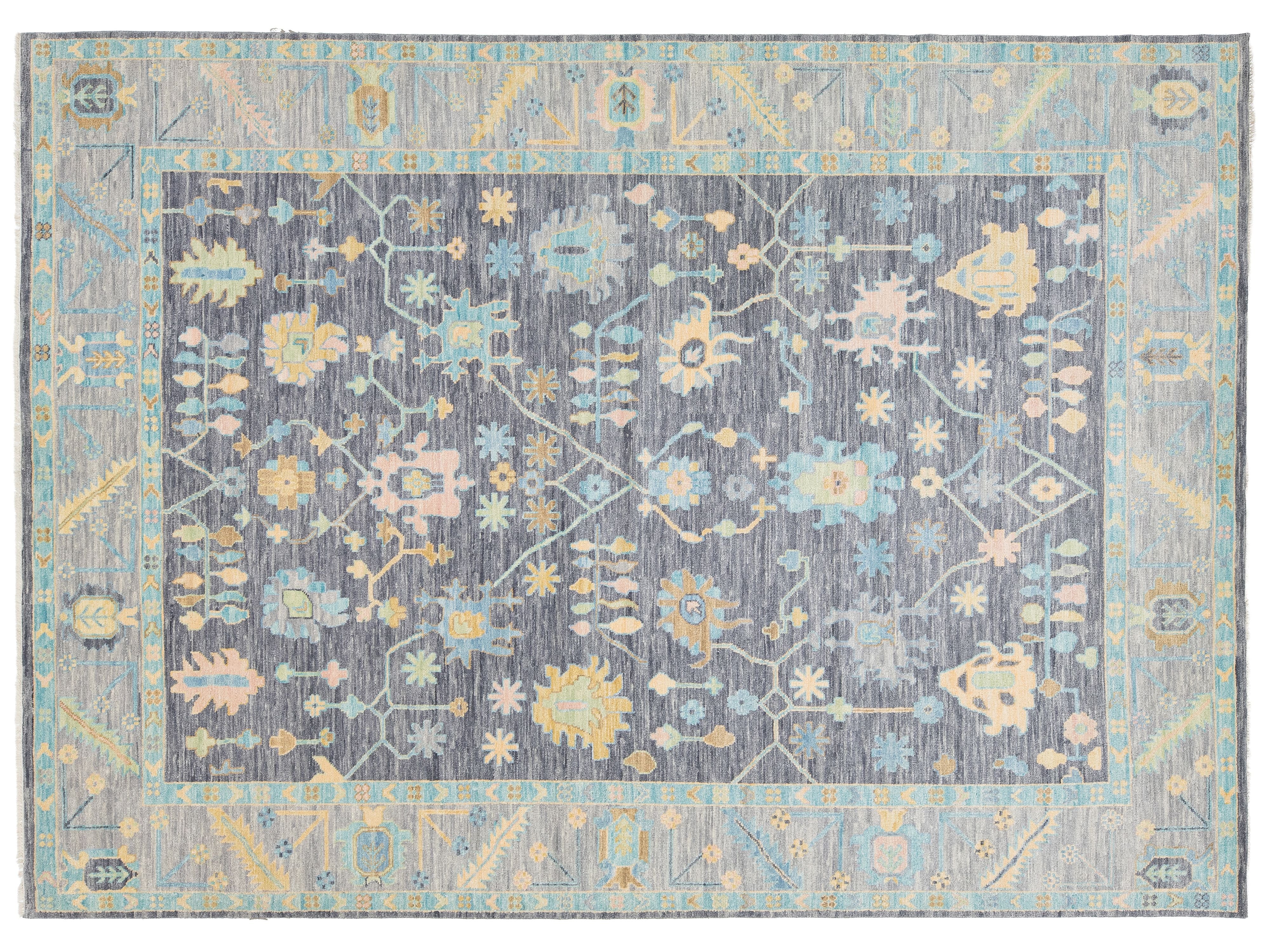 A rectangular area rug with a distressed traditional pattern, featuring a central field of charcoal gray with light blue, beige, and yellow floral motifs, surrounded by a light blue border.