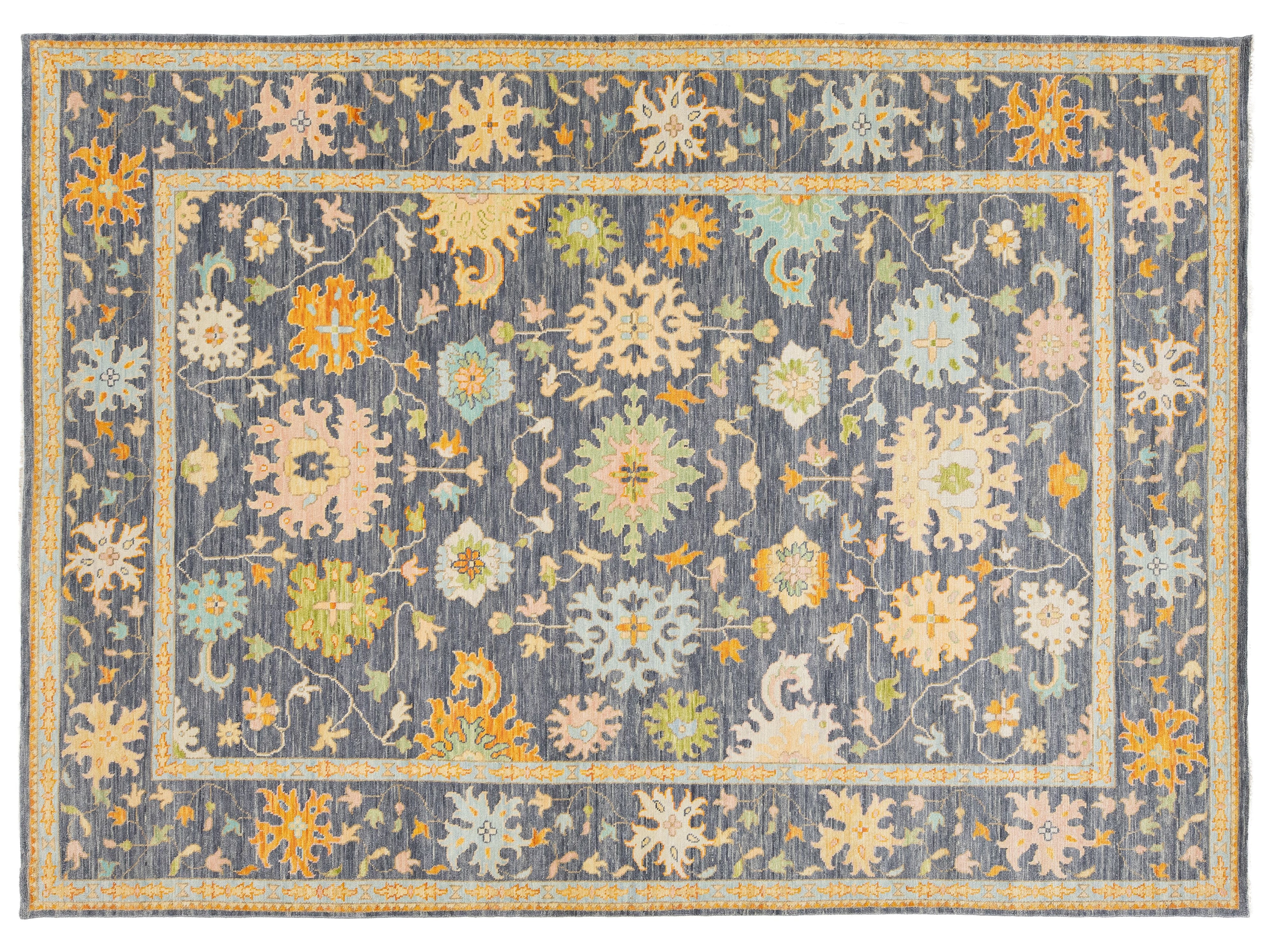 A rectangular area rug with a traditional floral pattern, featuring a slate blue-gray background with cream, mustard yellow, and light green motifs.
