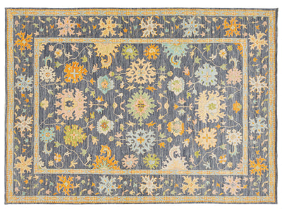 A rectangular area rug with a traditional floral pattern, featuring a slate blue-gray background with cream, mustard yellow, and light green motifs.