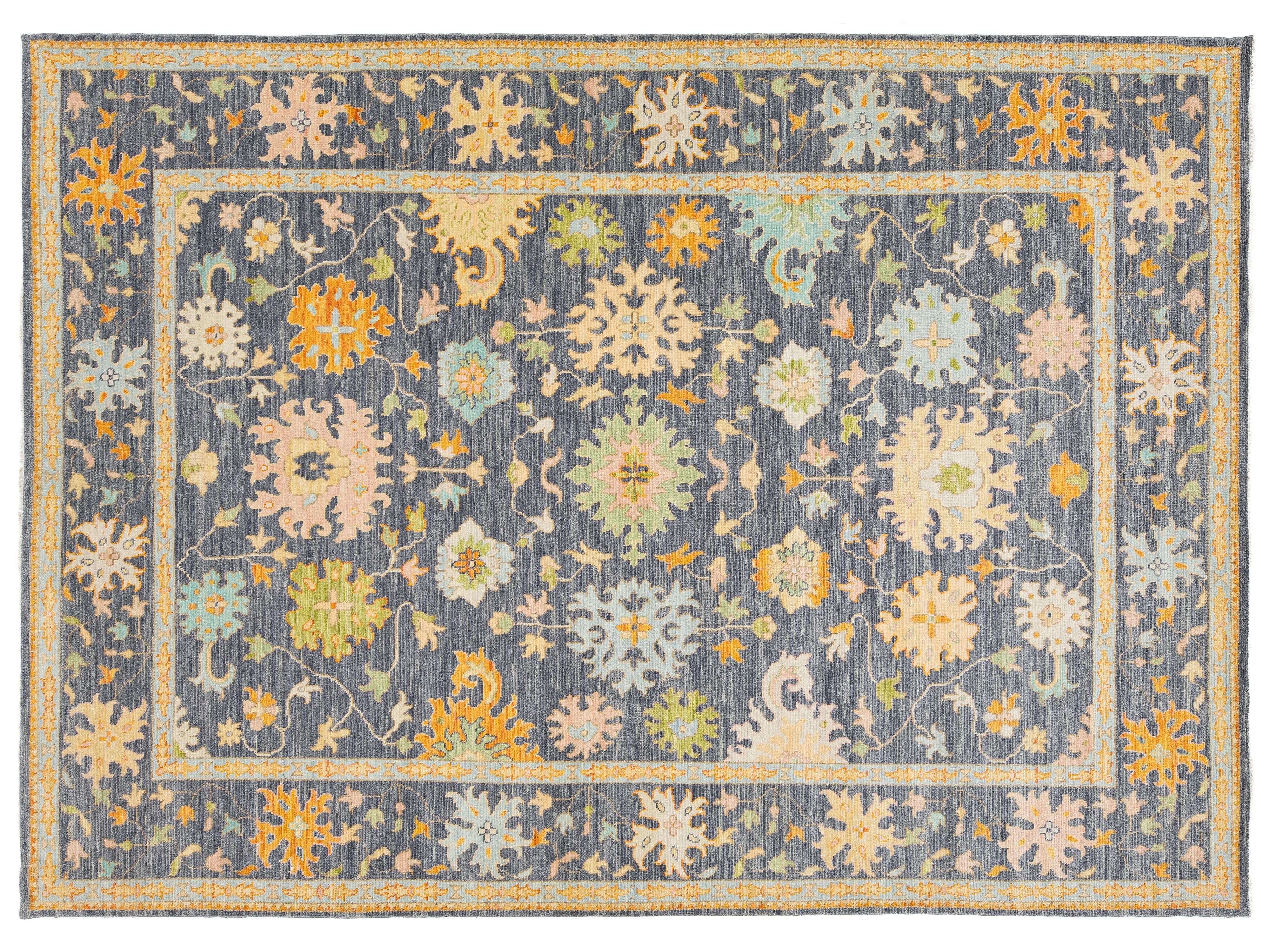 A rectangular area rug with a traditional floral pattern, featuring a slate blue-gray background with cream, mustard yellow, and light green motifs.