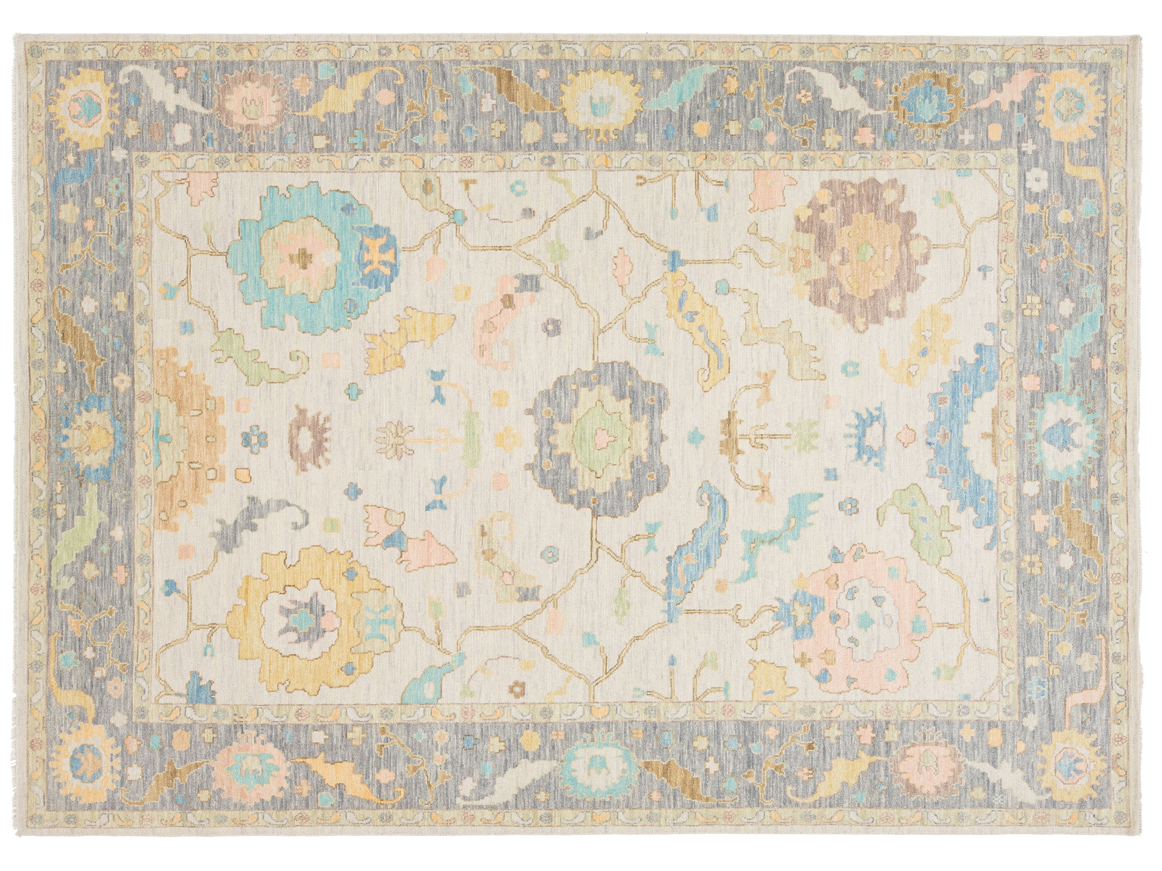 A rectangular area rug with an intricate traditional floral pattern in soft pastel colors including blue, yellow, pink, and green on a cream background, surrounded by a dusty blue border.