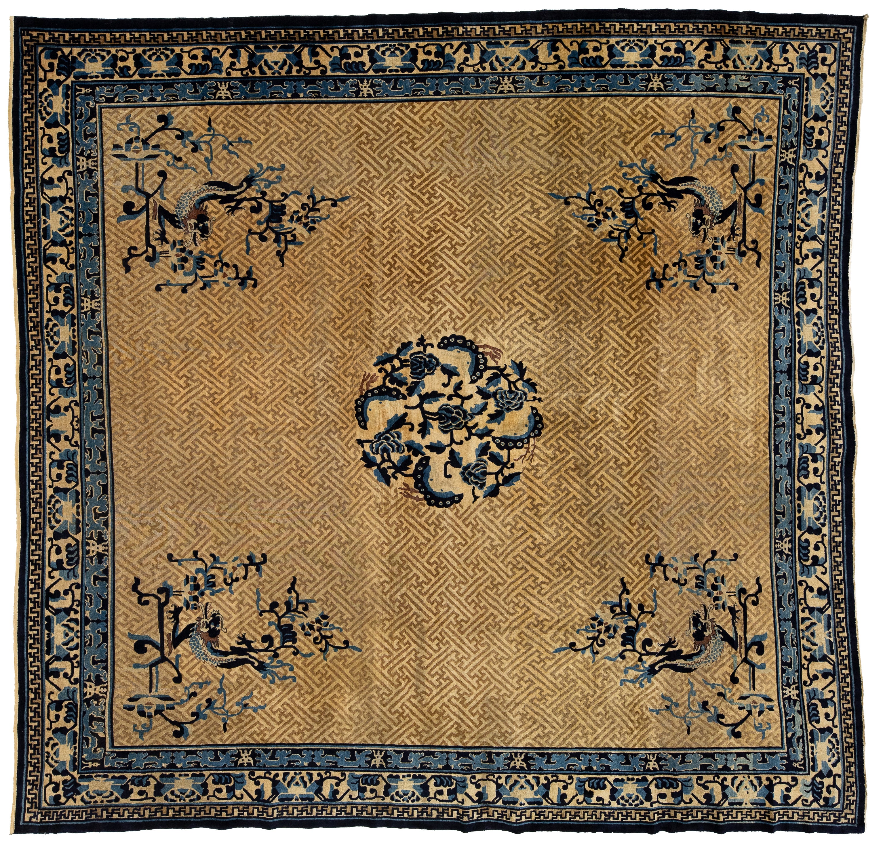 A square antique oriental rug with a tan and gold background, featuring a central floral medallion, four corner floral motifs, and a detailed blue and black border.