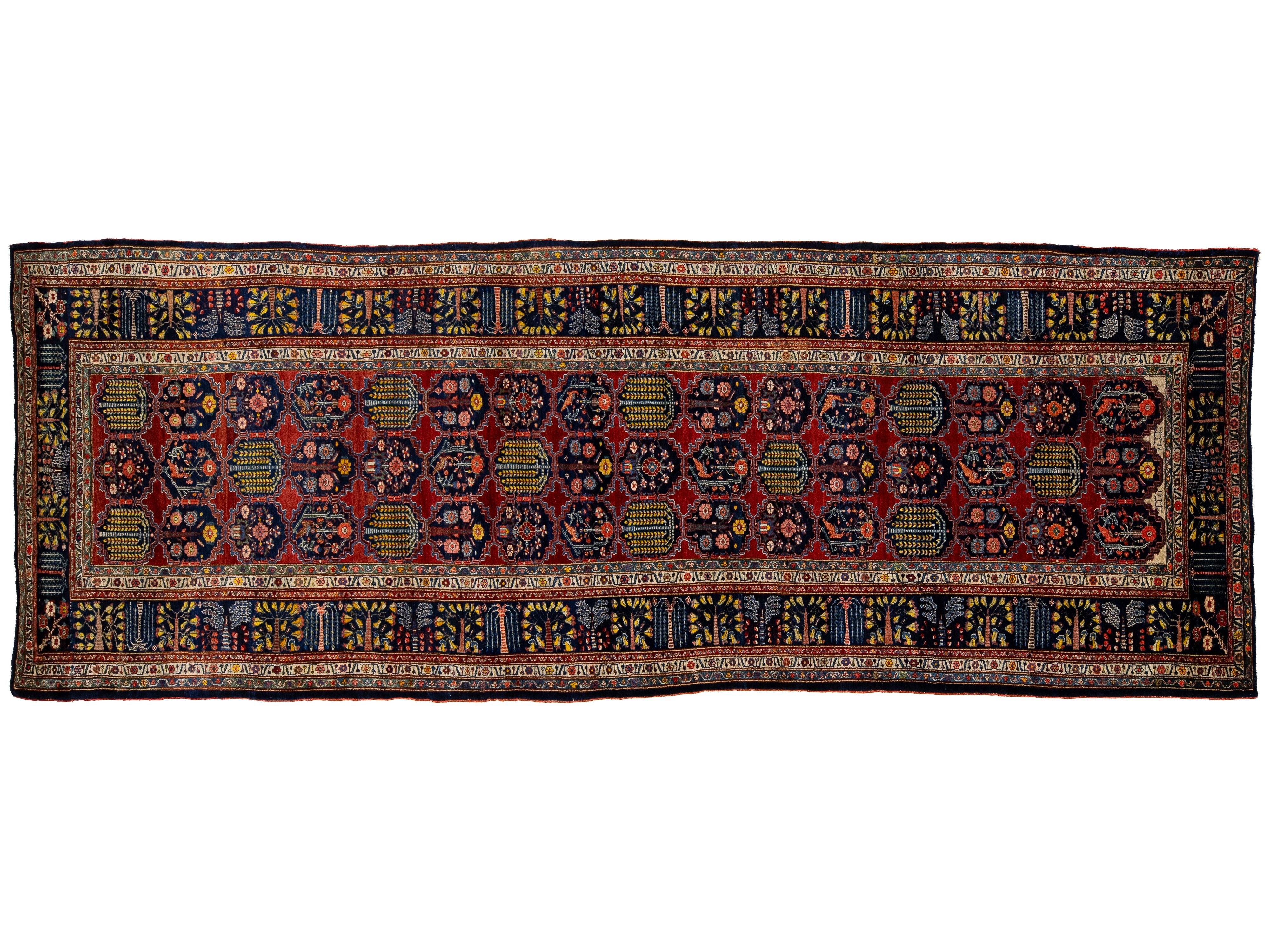 A traditional Persian-style runner rug with a deep red field, intricate blue, yellow, and black geometric and floral motifs, and a detailed border.