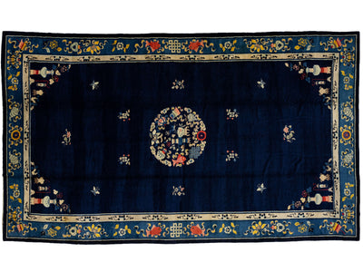 A rectangular navy blue rug with a central floral medallion, surrounded by small floral motifs and a decorative border in beige, blue, red, and yellow.
