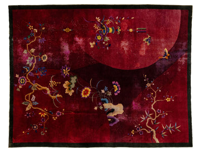 A square red textile or rug with a black border and embroidered floral motifs in gold, blue, purple, and yellow, plus a large pale red circular shape in the upper right.