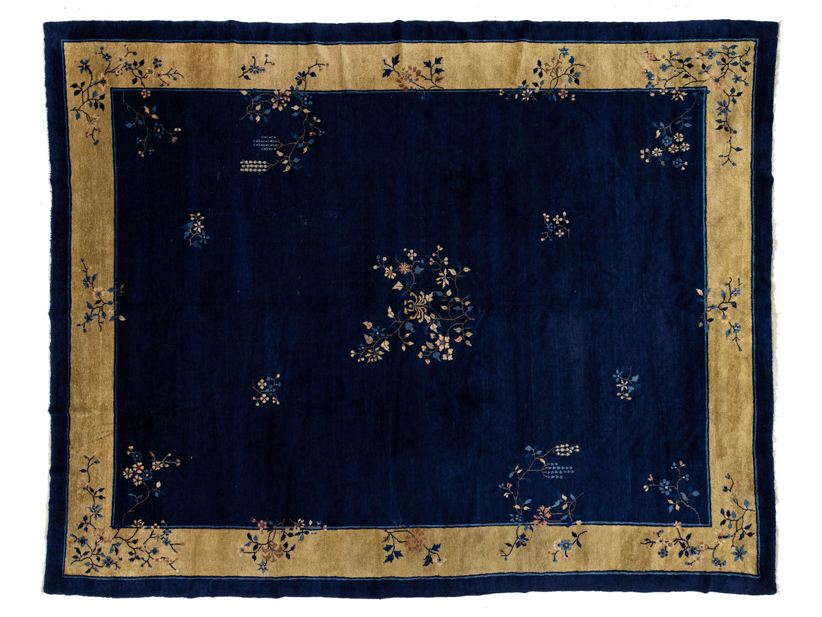 A rectangular Chinese navy blue rug with a wide tan border and delicate floral motifs.