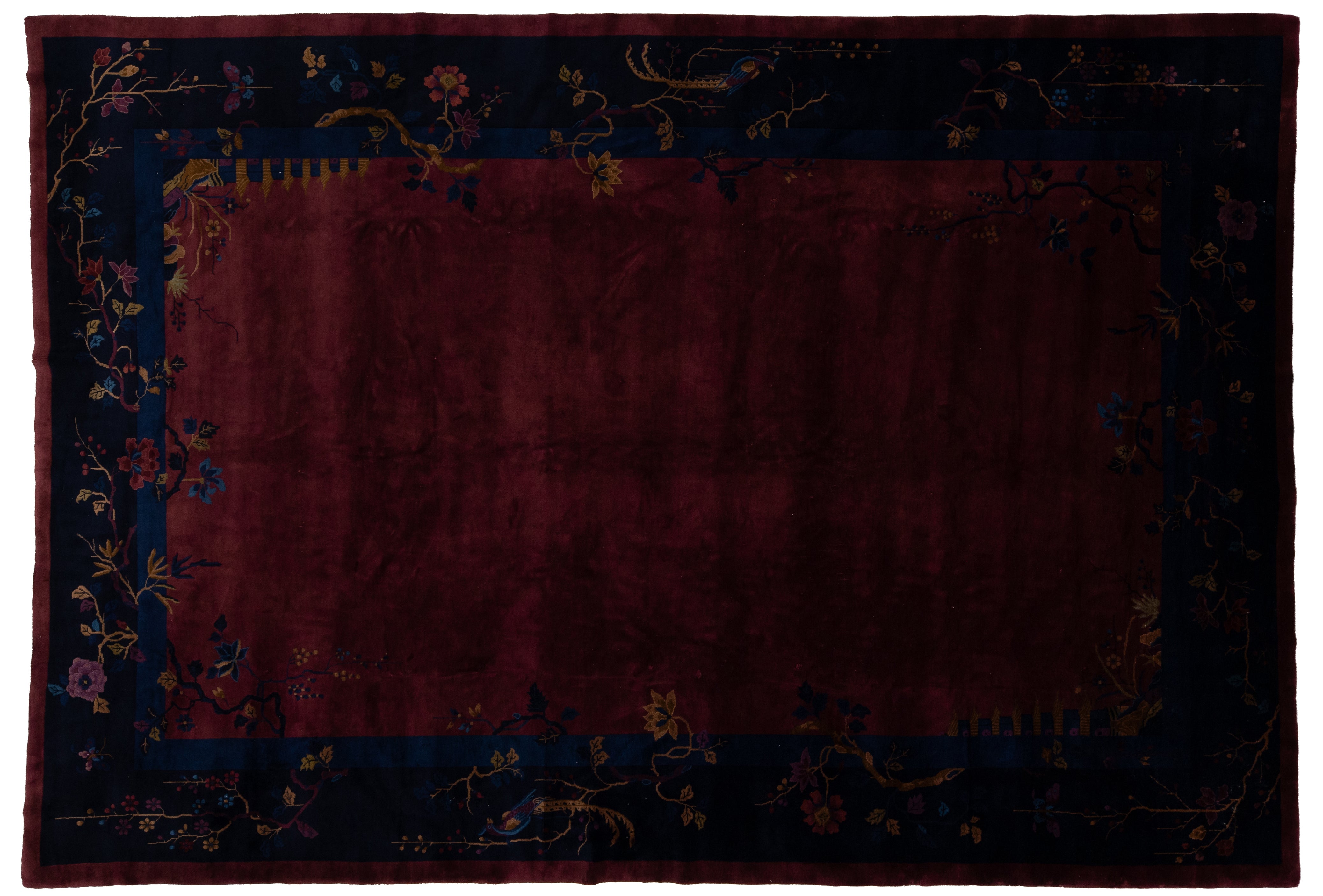 A rectangular area Chinese rug with a deep burgundy center field and a dark navy blue border decorated with floral and vine motifs in muted gold, pink, and blue tones.