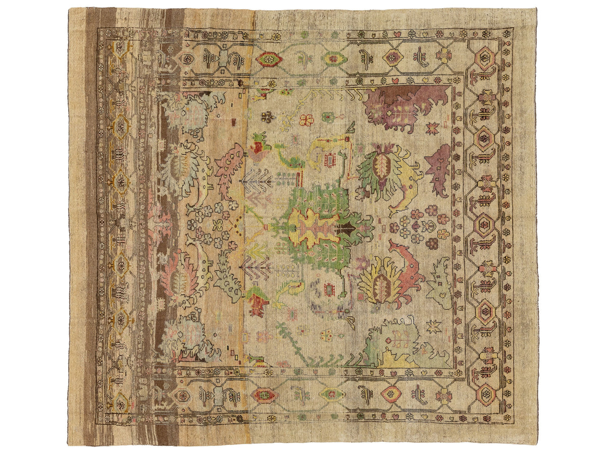 A square vintage area rug with a distressed, faded design. The rug features a beige and brown base with a central medallion and borders decorated with muted floral and geometric motifs in green, pink, yellow, and purple.