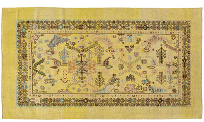 A rectangular hand-knotted wool rug with a yellow border and a central field featuring a multicolor folk-art pattern of trees, animals, and geometric motifs.
