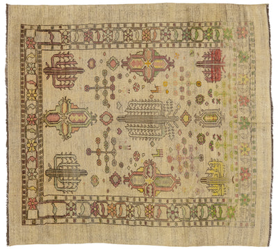 A square vintage wool rug with a distressed beige base and a complex geometric pattern in muted shades of red, green, yellow, and brown.