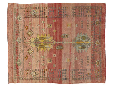A rectangular vintage-style area rug with a muted red and pink field, featuring a central medallion, geometric borders, and small floral motifs in beige, yellow, and light blue.