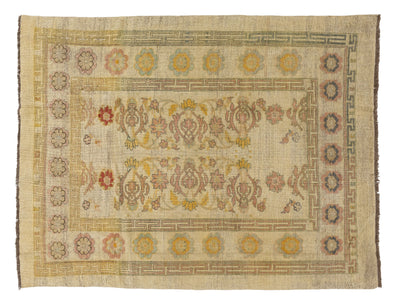 An vintage-style rectangular area rug with a distressed cream-beige field, featuring a central floral medallion motif and a decorative border with muted yellow, red, and blue accents.