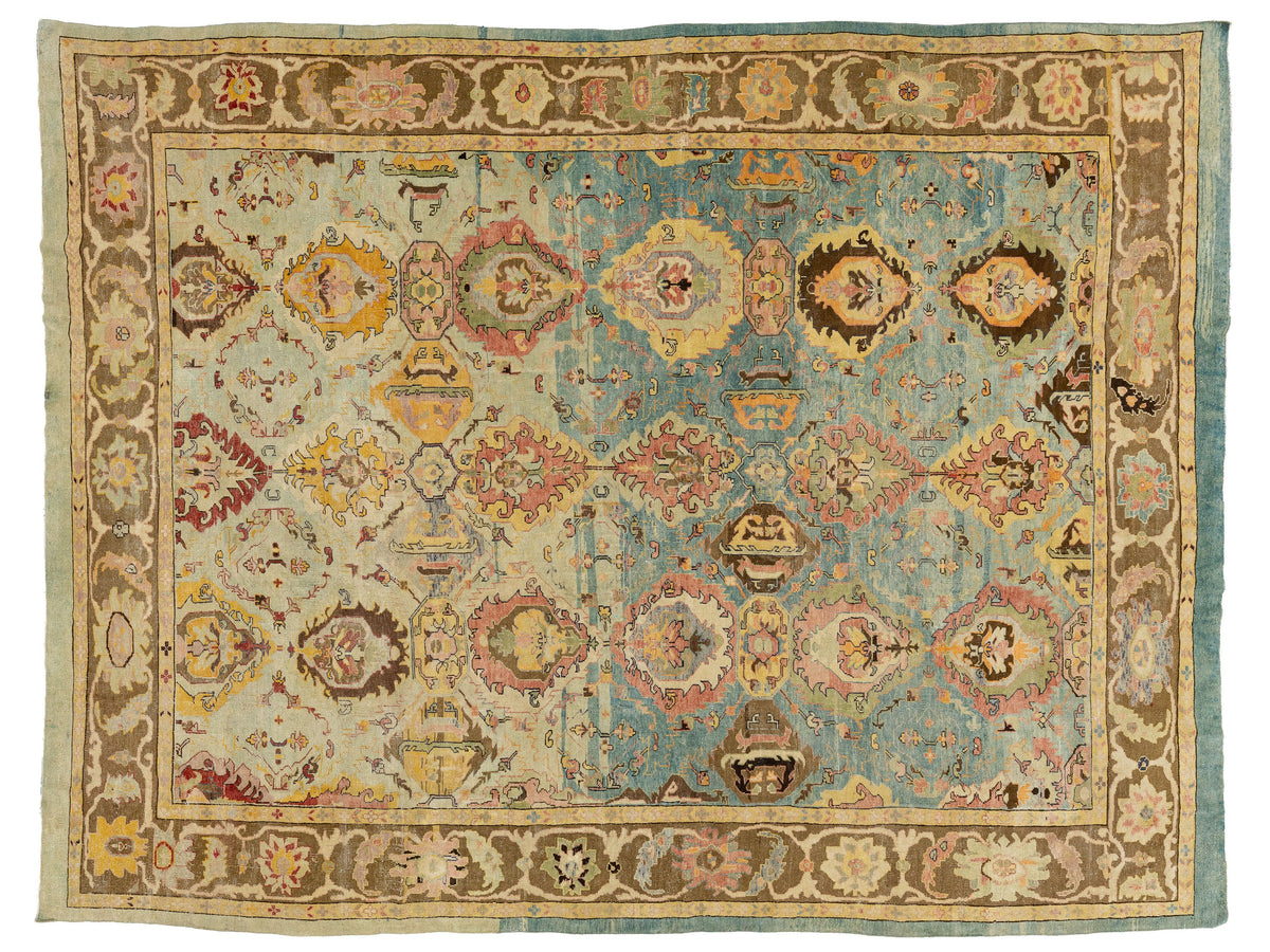 A rectangular vintage-style area rug with a distressed medallion pattern, featuring a light blue center field, beige and brown borders, and accents of pink, yellow, and green.